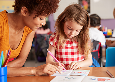Teacher help a school girl in writing note in a classroom